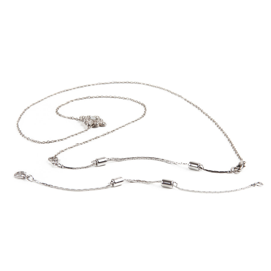 One silver adjustable necklace extender laid out in front of a silver necklace with attached silver adjustable necklace extender.