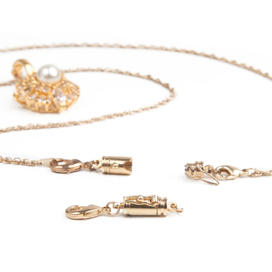 Goldtone small magnetic clasp with a safety catch on the side in front of a gold and pearl necklace with attached small magnetic clasp with a safety catch on one side.