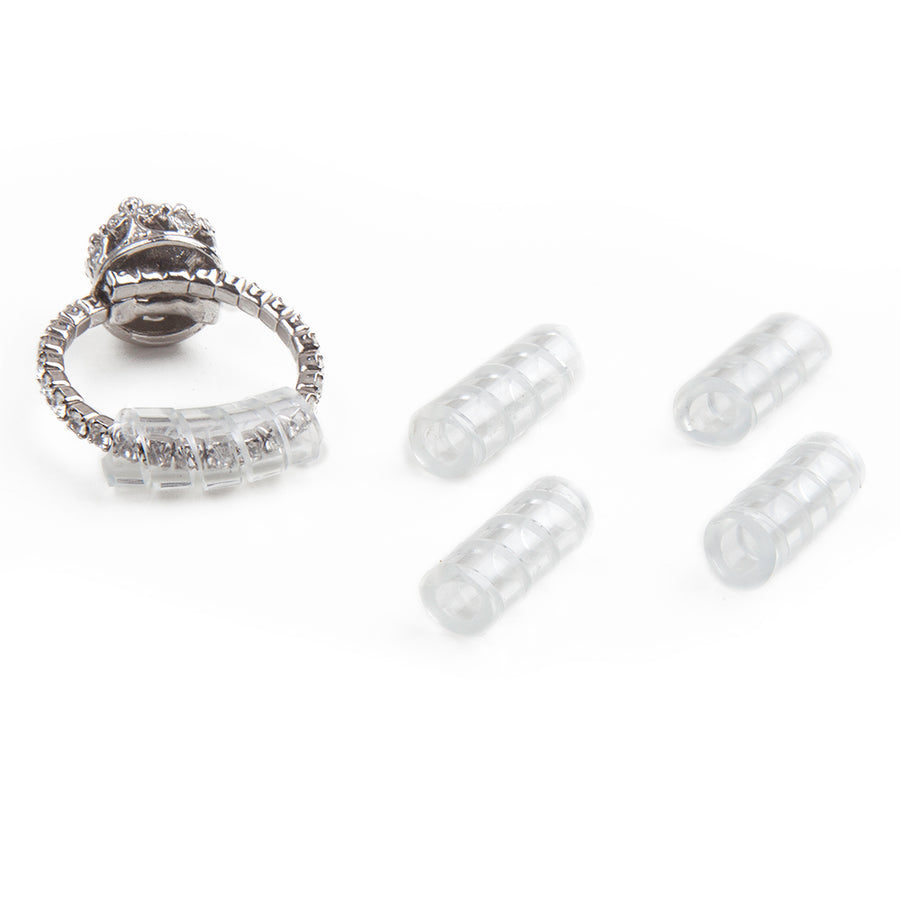 four clear, spiral-cut tubes that are spiral ring size adjusters next to a silver diamond ring with a spiral-cut sizer in use.