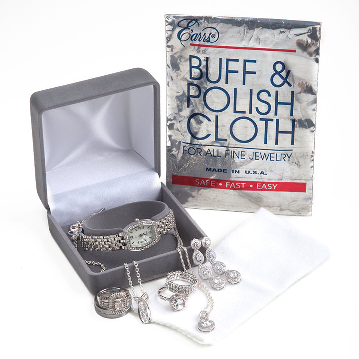an open box for wrist watches with diamond dangle earrings, a diamond pendant necklace, and diamond rings with a buff and polish cloth from earrs inc next to it and a pouch to store cloth against a white background