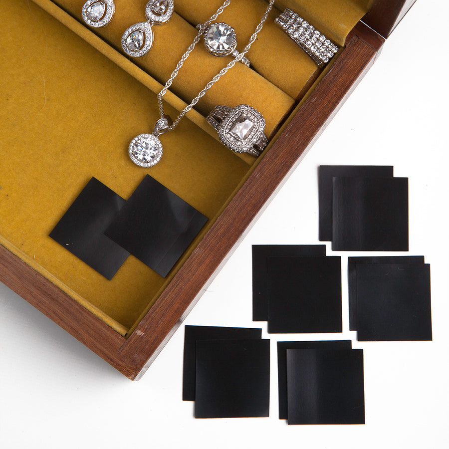 An open jewelry box with green yellow  felt featuring anti tarnish squares from earrs inc and some diamond dangle earrings, a diamond pendant necklace, and two styles of diamond earrings