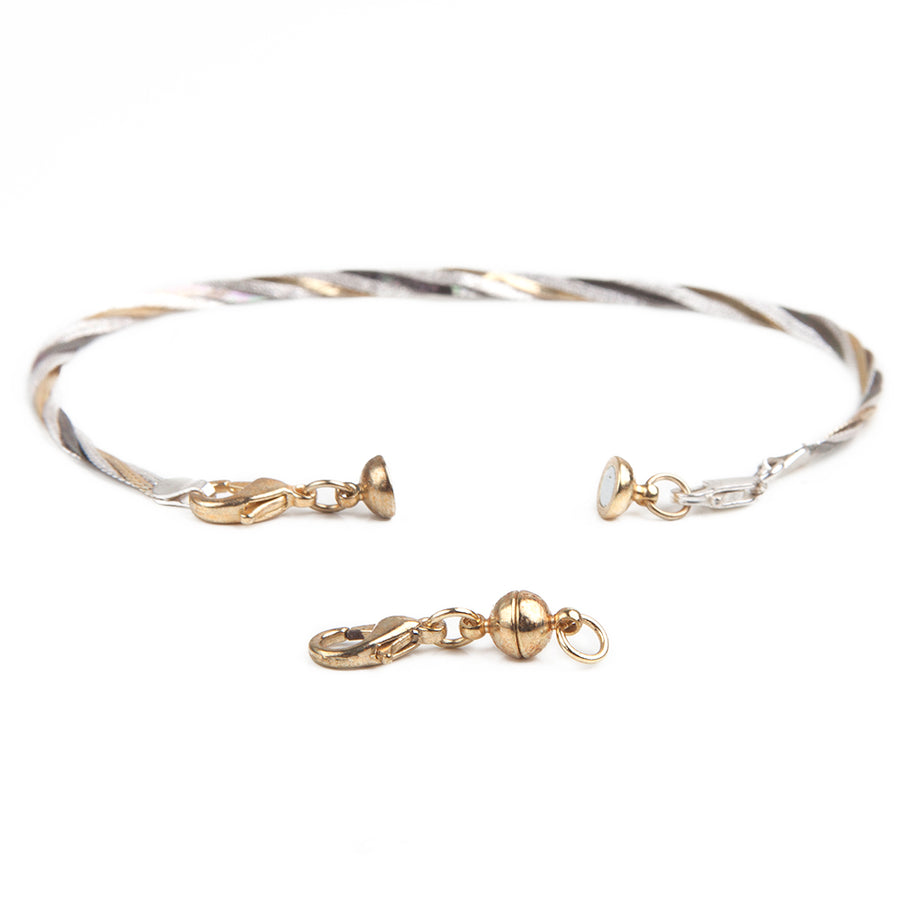 small gold sphere magnetic jewelry clasp in front of a gold and silver bracelet with attached small gold sphere magnetic clasp.