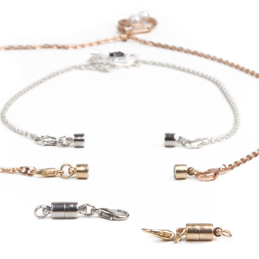 Two small barrel magnetic clasps in silver and gold in front of two necklaces in gold and silver with attached small barrel magnetic clasps.