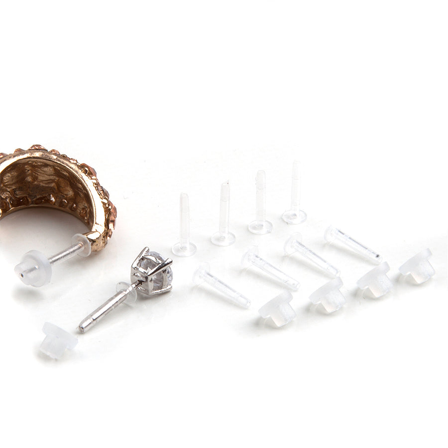 Clear earring sleeves with earring backs laid out next to a gold half-hoop and diamond stud showing how the earring sleeves and backs are placed on an earring.