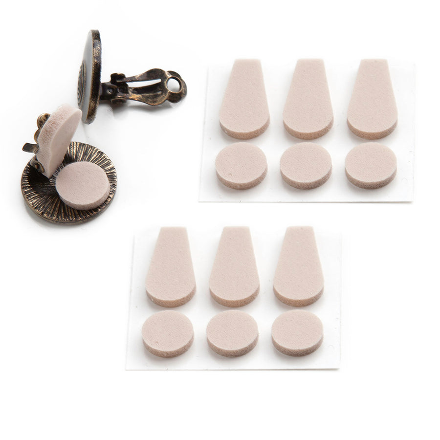two sheets of foam pads containing three paddle shaped pads and three dot shaped pads next to a pair of clip on earrings where one earring is displaying the foam pads in the correct use against a white background