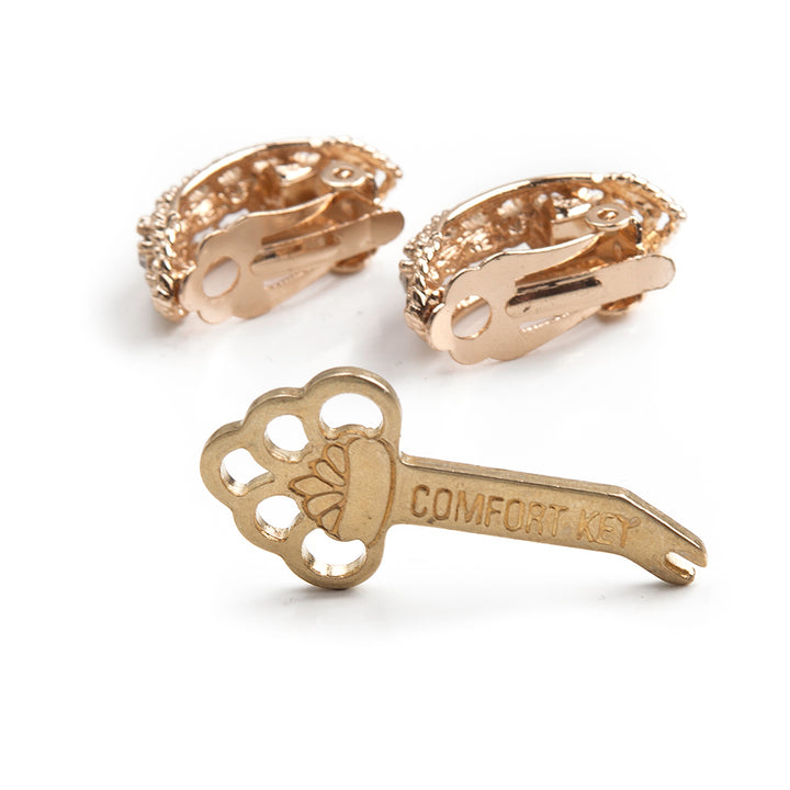 one gold Tension Key, labeled comfort key, on its edge in front of a pair of leverback clip earrings.