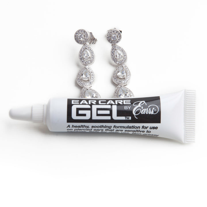 ear care gel tube from earrs inc in from of a pair of diamond dangle earrings against a white background