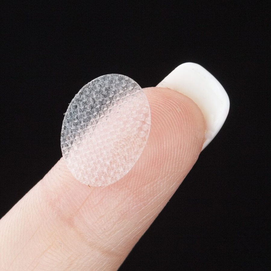 A finger with a long nail, showing the surface of a lobe saver adhesive patch.